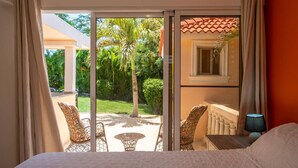 A bedroom with a bed, a nightstand, a lamp, and a view of a patio with chairs and a table. - Casa linda Villa 918 (Sosúa)