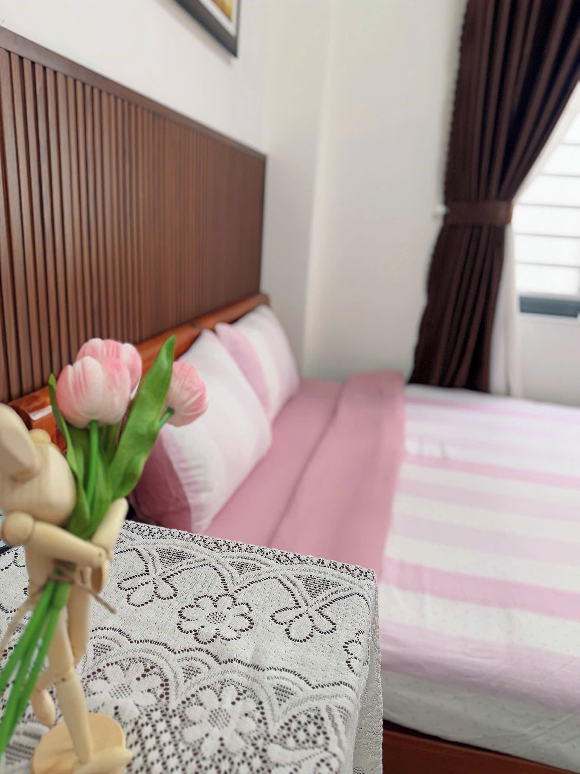 A bed with a wooden headboard, a pink and white striped bedspread, and a white lace-patterned pillow.
