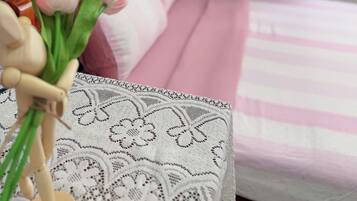 A bed with a wooden headboard, a pink and white striped bedspread, and a white lace-patterned pillow.