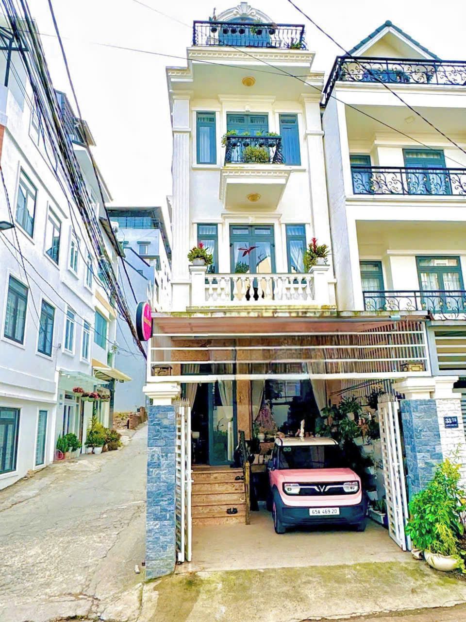 A multi-story residential building with a covered entrance, potted plants, and a parked car.