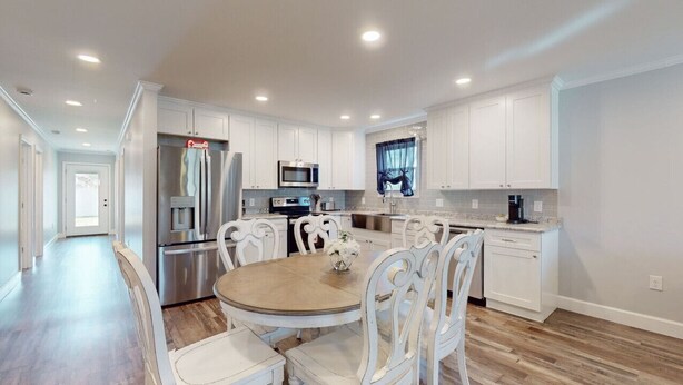 A modern kitchen with white cabinetry, stainless steel appliances, and a round dining table with white chairs.