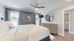 A bedroom with a bed, a ceiling fan, a dresser, a mirror, and a view of the outside.