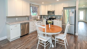 Una cocina moderna con armarios blancos, una mesa de comedor de madera y un refrigerador de acero inoxidable.