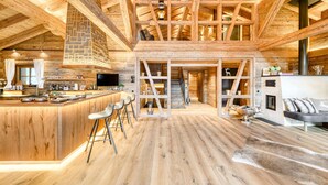 A spacious wooden interior with a high ceiling, a central staircase, and a bar area with stools. - Chalet GM in Brand With 5 Bedrooms and 4 Bathrooms (Brand)