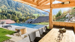 A wooden deck with a pool, wicker chairs, and a table with a decorative centerpiece. - Chalet GM in Brand With 5 Bedrooms and 4 Bathrooms (Brand)