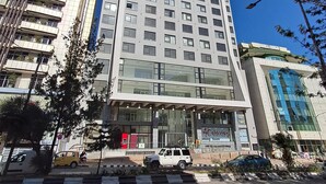 Un hotel de varios pisos con fachada moderna de vidrio, una entrada destacada y un estacionamiento al frente.