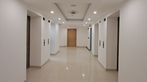 Un largo pasillo bien iluminado, con paredes blancas y piso de baldosas, que conduce a una puerta al final.