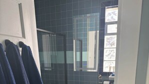 Un bany amb una cabina de dutxa de vidre, un vàter blanc i una paret amb rajoles blaves.