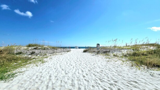 A sandy beach path leading to the ocean with a wooden fence on either side. - Sunchase 204 | Pool & Hot Tub | Steps to the Beach (Gulf Shores)