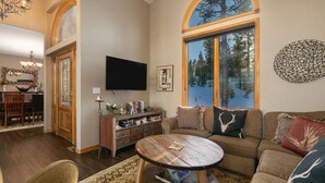 A cozy living room with a large window, a flat-screen TV, a wooden coffee table, and a comfortable sofa. - Stunning Mountain Retreat W/Views|Private Hot Tub (Tabernash)