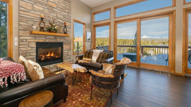 A spacious living room with a stone fireplace, leather furniture, and large windows offering a view of a snowy landscape. - Stunning Mountain Retreat W/Views|Private Hot Tub (Tabernash)