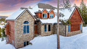 A large, multi-story stone and wood house with a snow-covered roof, surrounded by trees and a snowy landscape. - Stunning Mountain Retreat W/Views|Private Hot Tub (Tabernash)
