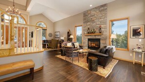 A spacious living room with a fireplace, a stone accent wall, and a large window offering a view of the outdoors. - Stunning Mountain Retreat W/Views|Private Hot Tub (Tabernash)
