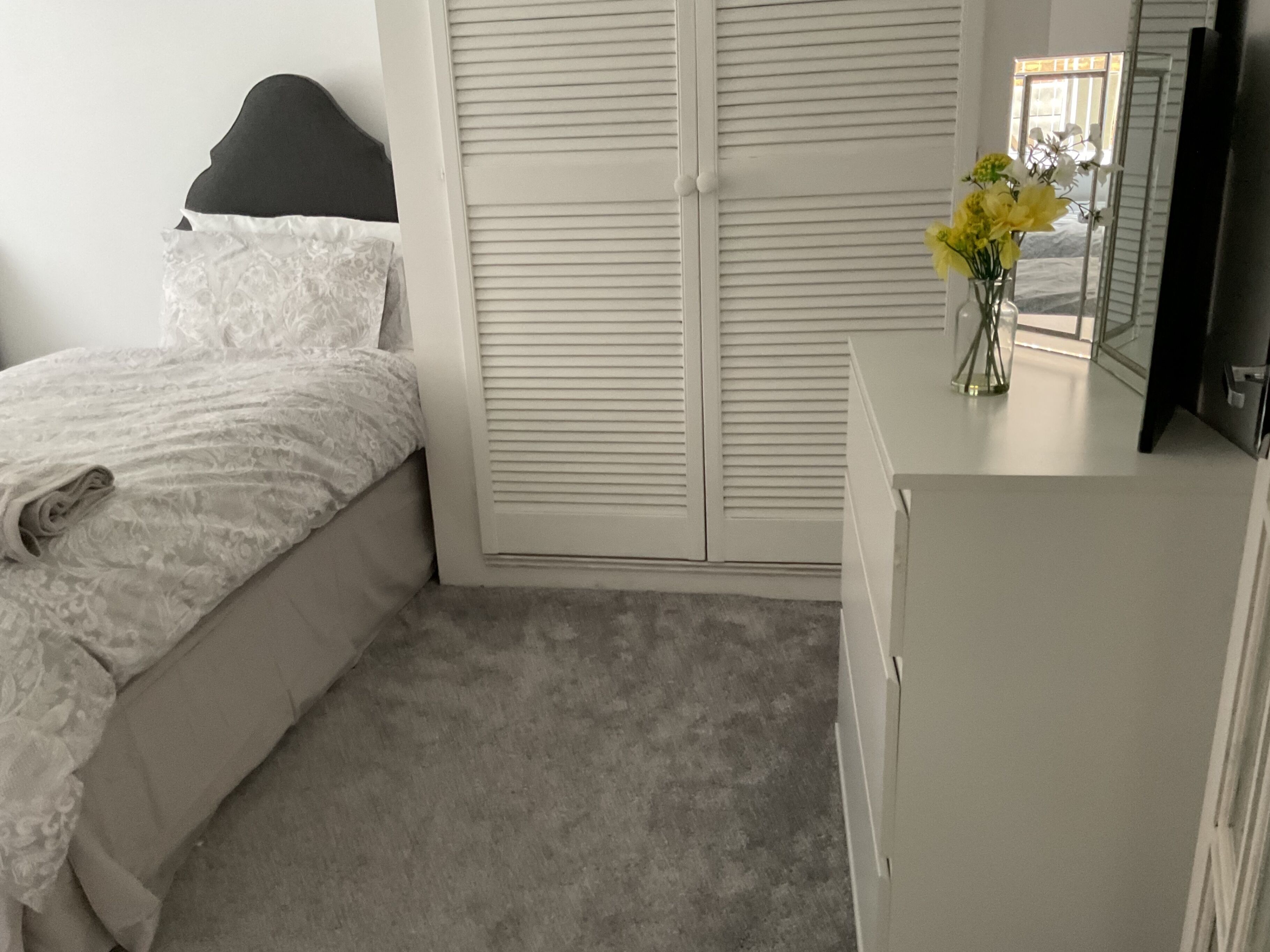 A bedroom with a bed, a dresser, a mirror, and a window with blinds.