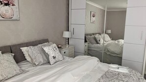 Een slaapkamer met een bed, nachtkastjes, een spiegel en een kledingkast.