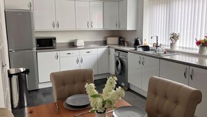 Een moderne keuken met witte kasten, een magnetron, een wasmachine en een eethoek met een tafel gedekt voor twee personen.