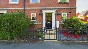 A red brick house with a black gate, a front door, and a small garden with red flowers. - Sleeps6- FamilyFriendly- FreeParking- 3Br (Stafford)