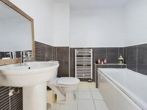 Bathroom features a pedestal sink, toilet, and bathtub, set against a backdrop of black and white striped tiles.