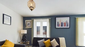A living room with a dark sofa, a side table with a lamp, and two framed pictures on the wall. - Sleeps6- FamilyFriendly- FreeParking- 3Br (Stafford)