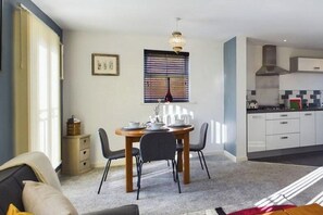 Cozy living area with a dining table for two, featuring a window with blinds and a chandelier.
