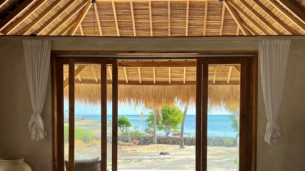 Un dormitorio con una cama grande, vista al océano y techo de paja.