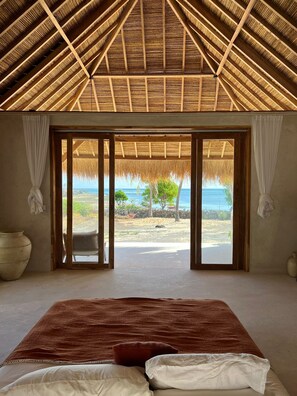 A bedroom with a large bed, a view of the ocean, and a thatched roof. - Rote Beach Bungalows (Rote Island)