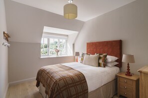A bedroom with a large bed, a window with a view, a nightstand, and a lamp.
