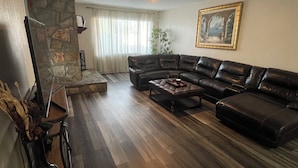 Ein Wohnzimmer mit Kamin aus Stein, einem schwarzen Ledersofa, einem Couchtisch und einem Deckenventilator.