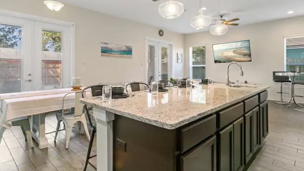 Una cocina moderna con una isla grande, luces colgantes y un comedor con sillas.