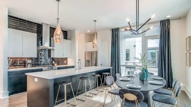 A modern kitchen with a central island, bar stools, and a dining area with a round table and chairs. - Encore Estates - Rooftop deck & skyline views (Nashville)