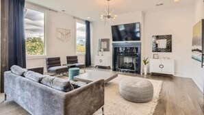 A modern living room with a grey sofa, a coffee table, a fireplace, and a television. - Encore Estates - Rooftop deck & skyline views (Nashville)