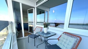 A balcony with a glass table, two chairs, a vase with flowers, and a view of the city. - FB12.06 - Apartment for 2 persons with sea view, swimming pool and sauna - (Cuxhaven)