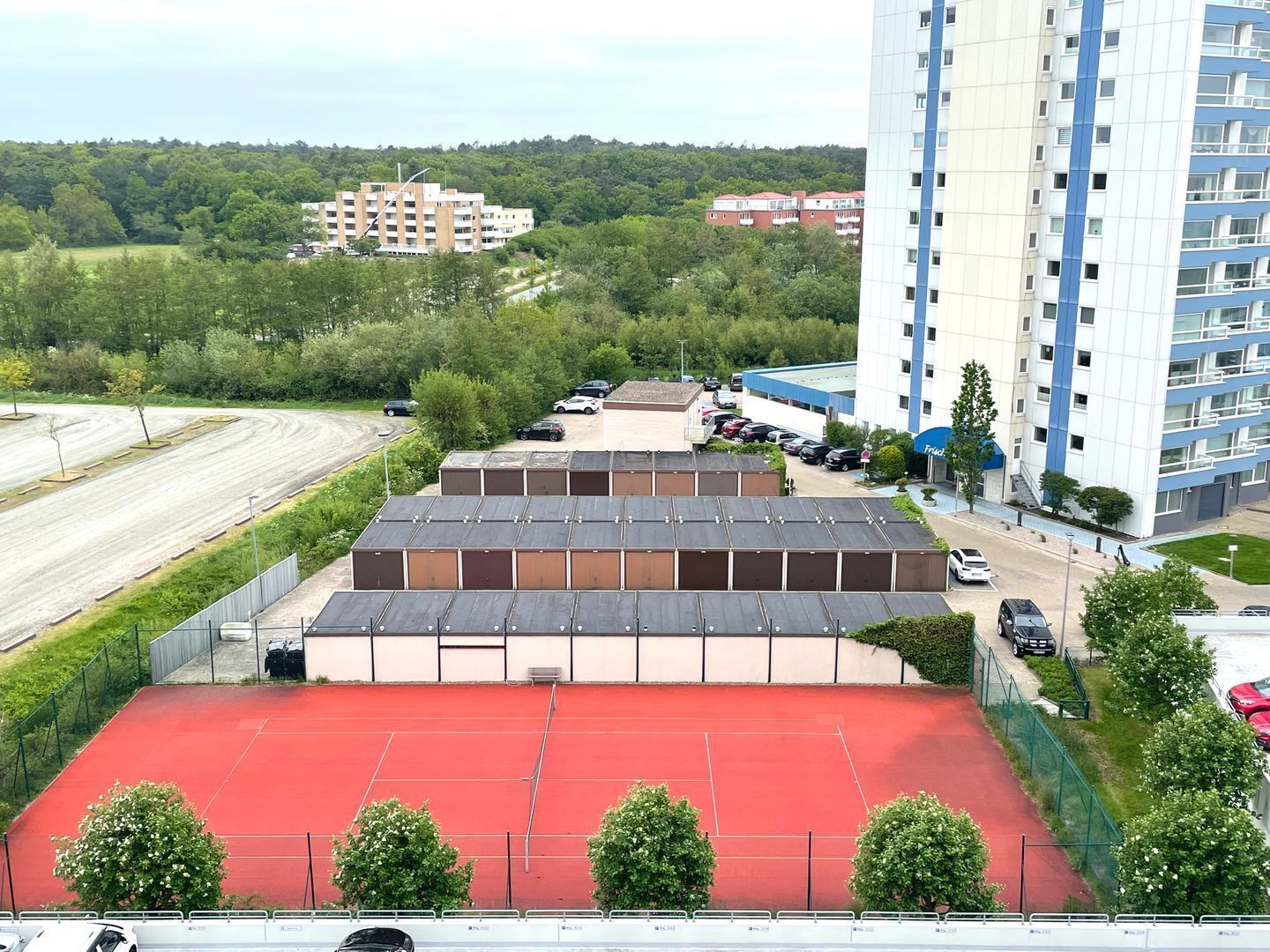 Un immeuble à plusieurs étages doté d’un parking et d’un terrain de sport rouge.