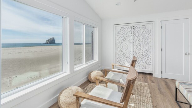 Een kamer met grote ramen met uitzicht op een strand, een plafondventilator en een decoratief wit paneel.