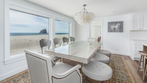 Een eetgedeelte met een glazen tafel, witte stoelen en uitzicht op het strand.