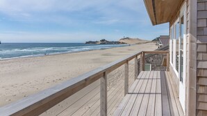 Een houten terras met uitzicht op een strand en een helder zicht op de oceaan en heuvels in de verte.