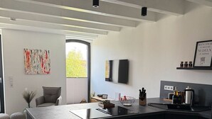 A modern kitchen with a large island, a dining area with a chair, and a view of the outdoors. - Frieda - Modern Vacation Rental in Rysum near Greetsiel, 92 m²/6 people - Hof Van (Rysum)