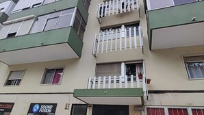 A multi-story building with a green and beige facade, a storefront with a sign for 'Sound Fusion,' and a gated entrance. - Lisbon spacious T2 in Damaia, Lisbon (Amadora)