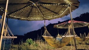 A hammock under a large umbrella with string lights, set in a natural outdoor environment. - Shobha Farmhouse (Murud)