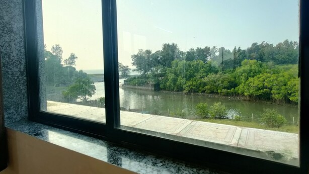 A view through a window of a river with a bridge, surrounded by dense greenery. - Shobha Farmhouse (Murud)