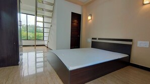 A bedroom with a bed, a wooden wardrobe, a window with a view, and a door. - Shobha Farmhouse (Murud)