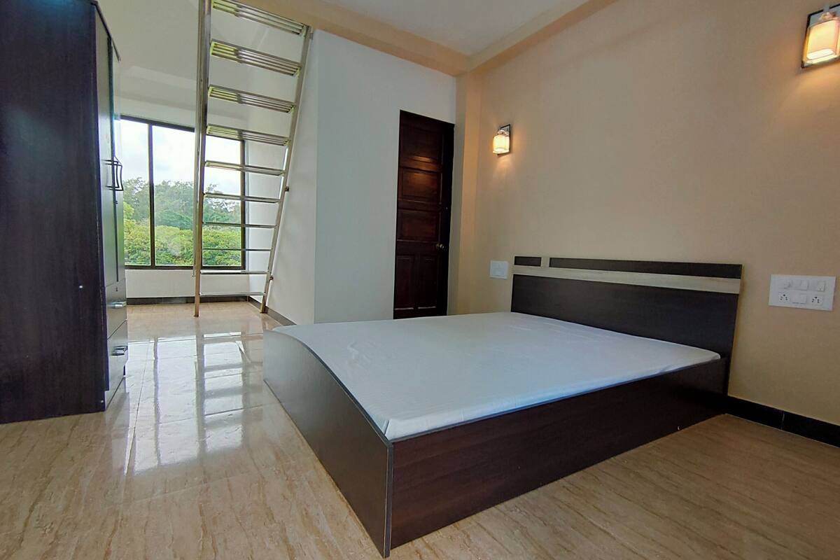 A bedroom with a bed, a wooden wardrobe, a window with a view, and a door.