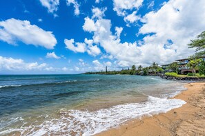 A beach with clear blue water, a sandy shore, and a building with a view of the ocean. - Direct Oceanfornt 2BD 2B Amazing Views AC Pool Steps to Sandy Beach- Kahana Village 3 (Lahaina)