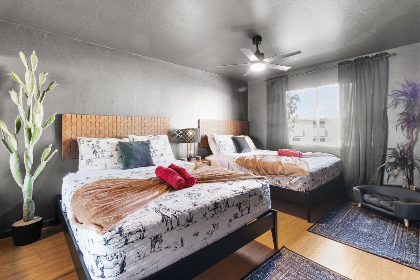 Habitación de hotel con dos camas, ventilador de techo, ventana con cortinas y una planta en maceta.