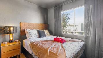 Habitación de hotel con cama, lámpara de noche, mesita de noche y ventana con cortinas.