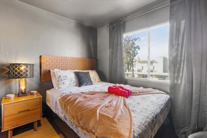 A hotel room with a bed, a bedside lamp, a nightstand, and a window with curtains.