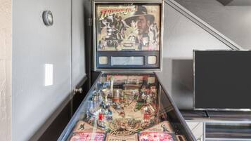 Una máquina de pinball con diseño vintage, ubicada en una habitación con una escalera y un televisor.