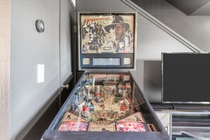 A pinball machine with a vintage design, located in a room with a staircase and a television.