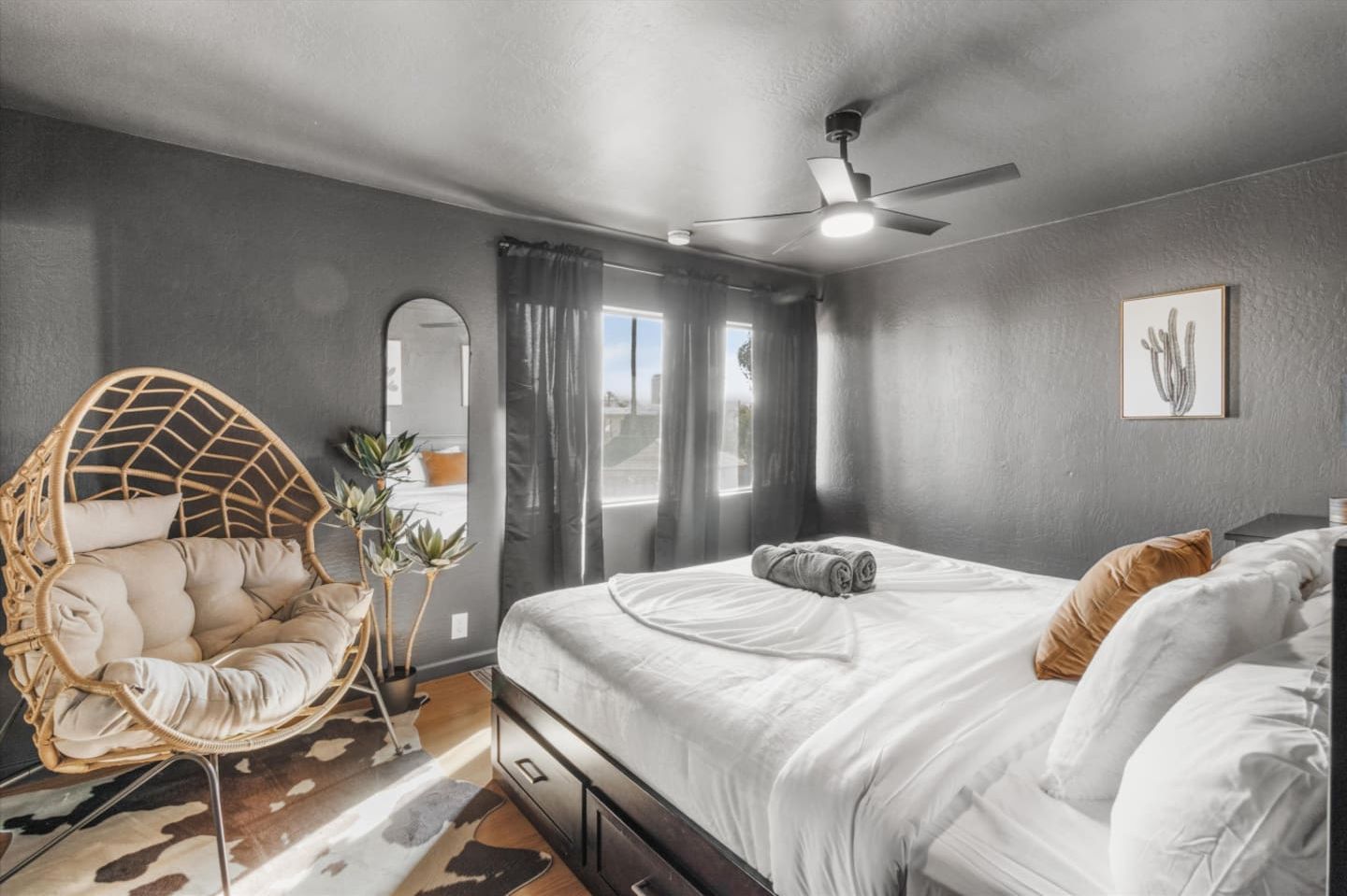A bedroom with a bed, a ceiling fan, a hanging chair, and a window with curtains.