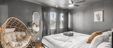 A bedroom with a bed, a ceiling fan, a hanging chair, and a window with curtains.